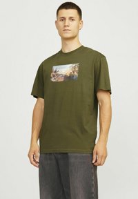 Oliven grøn bomuld T-shirt med korte ærmer og løs pasform, med et trykt grafik, der viser en naturscene på forsiden.