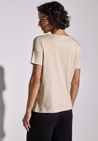 Camiseta beige de manga corta con escote redondo, hecha de una tela suave, con un corte relajado y dobladillo recto, combinada con pantalones negros.