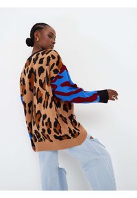 Maglione a stampa leopardata marrone, maniche blu con accenti rossi, vestibilità rilassata, texture lavorata a maglia, abbinato a jeans leggeri blu chiaro strappati.