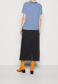 Camiseta de algodón a rayas azul y blanca, falda maxi de mezclilla negra con abertura, y botas altas de rodilla naranjas brillantes con tacones cuadrados.