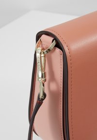 Gros plan sur un coin d’un sac à main en cuir rose et marron avec un fermoir métallique doré et une attache de sangle.