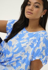 Blue floral short-sleeve top with white flower patterns, round neckline, lightweight fabric, and smooth texture.
