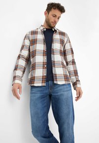 Kariertes Hemd in Beige-, Braun- und Blautönen, aus Stoff mit strukturiertem Muster, im Button-Down-Stil, über einem marineblauen T-Shirt getragen.