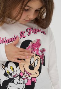 Camicetta bianca a maniche lunghe con una grafica colorata di un personaggio dei cartoni animati con un fiocco di paillettes rosa, accompagnato da un gatto dei cartoni.