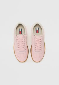 Ljust rosa sneakers med en slät ovandel och gummisula, utrustad med klassiska snören och en märkesetikett på insidan.