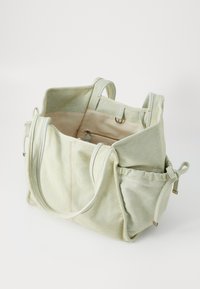 Grande borsa in tela di colore verde chiaro con due manici, tasche interne, tasche laterali con coulisse e dettagli di cucitura a contrasto.