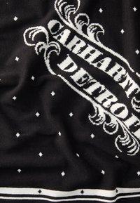 Tessuto a maglia nero con testo bianco ed elementi decorativi. Il motivo include stelle e strisce orizzontali nella parte inferiore.