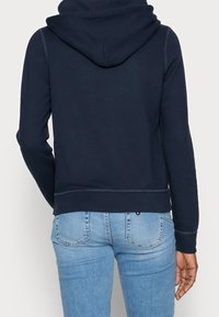 Felpa in cotone blu navy vista da dietro, con cappuccio regolabile e polsini a coste. Abbinata a jeans azzurri.