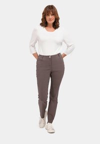 Un pantalon gris à coupe slim et taille haute, avec des poches avant et une fermeture à bouton. Associé à une chemise blanche à manches longues et des baskets.