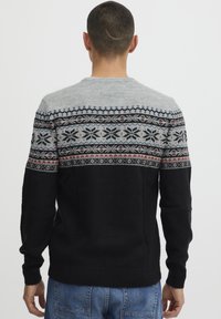 Pullover mit einem hellgrauen Oberteil und gestricktem Muster in Schwarz, Rot und Blau, das in durchgehende schwarze Ärmel und einen schwarzen Körper übergeht.