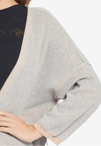 Lichtgrijze cardigan met een beige bies, met een losse pasvorm, brede mouwen en textiel met een structuur, die gedeeltelijk over een donker shirt hangt.
