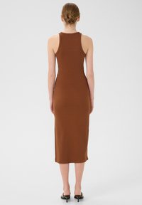 Abito midi marrone a costine, senza maniche, con una silhouette aderente, scollatura rotonda e orlo dritto, indossato con semplici tacchi neri.