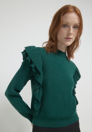 Green sweater featuring prominent ruffle detailing along the shoulders, made of textured fabric with a fitted silhouette and high neck.