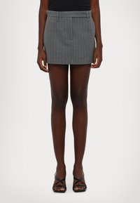 Mini-jupe grise à rayures avec passants de ceinture, design ajusté et silhouette structurée. Associée à des sandales à talons à lanières noires.