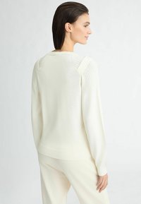 Pull crème avec des détails côtelés aux épaules, à manches longues et encolure arrondie, fabriqué en matériau tricoté doux.