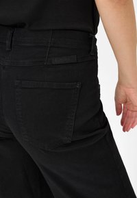 Pantaloni in denim nero con vita alta. Presentano due tasche posteriori, dettagli di cucitura e un'etichetta che indica il marchio.
