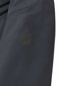 Granatowa kurtka wykonana z gładkiego, wodoodpornego materiału, z czarną naszywką z logo i minimalistycznym designem bez widocznych elementów metalowych.