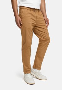 Tan chinos made of cotton blend, featuring flat front and side pockets, tailored fit, and straight legs, paired with white sneakers.