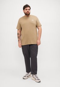 Kaki bomull t-skjorte med korte ermer og rund hals, kombinert med mørkegrå cargo bukser med doble sidelommer. Nøytrale sneakers.