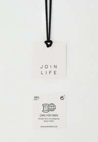 Étiquettes blanches attachées avec une ficelle noire. L'étiquette du haut indique "JOIN LIFE" ; celle du bas mentionne "PAPIER 100 % RECYCLÉ" avec des instructions d'entretien et un site web.