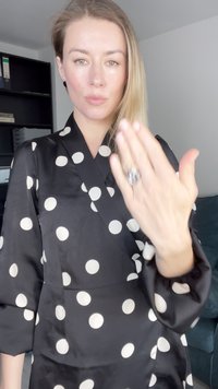 Blusa negra con lunares grandes blancos, que presenta un diseño de envoltura y mangas abullonadas. Se lleva un anillo llamativo en la mano.