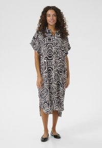 Abito camicia in tessuto leggero con un motivo astratto bianco e nero, maniche corte, spacchi laterali e una vestibilità rilassata.