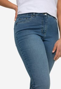 Modré džíny z denimu s priliehavým strihom, s polovičným pásom, prednými vreckami a hladkou textúrou. Ozdobené kovovými detailmi.