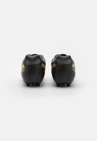 Las botas de fútbol negras presentan una parte superior de cuero suave con un talón texturizado y rayas doradas. La suela cuenta con múltiples clavos para una mejor tracción.
