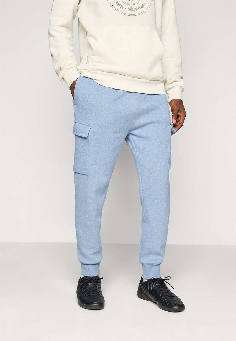 Light blue sweatpants made from soft fabric, featuring side pockets and ribbed cuffs. Paired with a cream hoodie and black sneakers.
