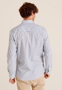 Lichtblauw shirt met een bloemenpatroon in roze, groen en paars. Lange mouwen, knoopsluiting bij de kraag en een afgeronde zoom. Gladde textuur.