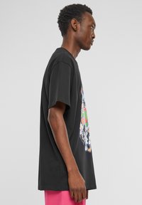 Sort bomulds t-shirt med et farverigt grafisk print af figurer på fronten. Korte ærmer, afslappet pasform, rund halsudskæring.