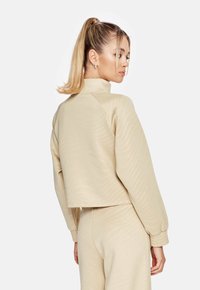 Beige cropped sweatshirt met een hoge kraag, geribde manchetten en een subtiele golfstructuur, gecombineerd met bijpassende onderkleding.