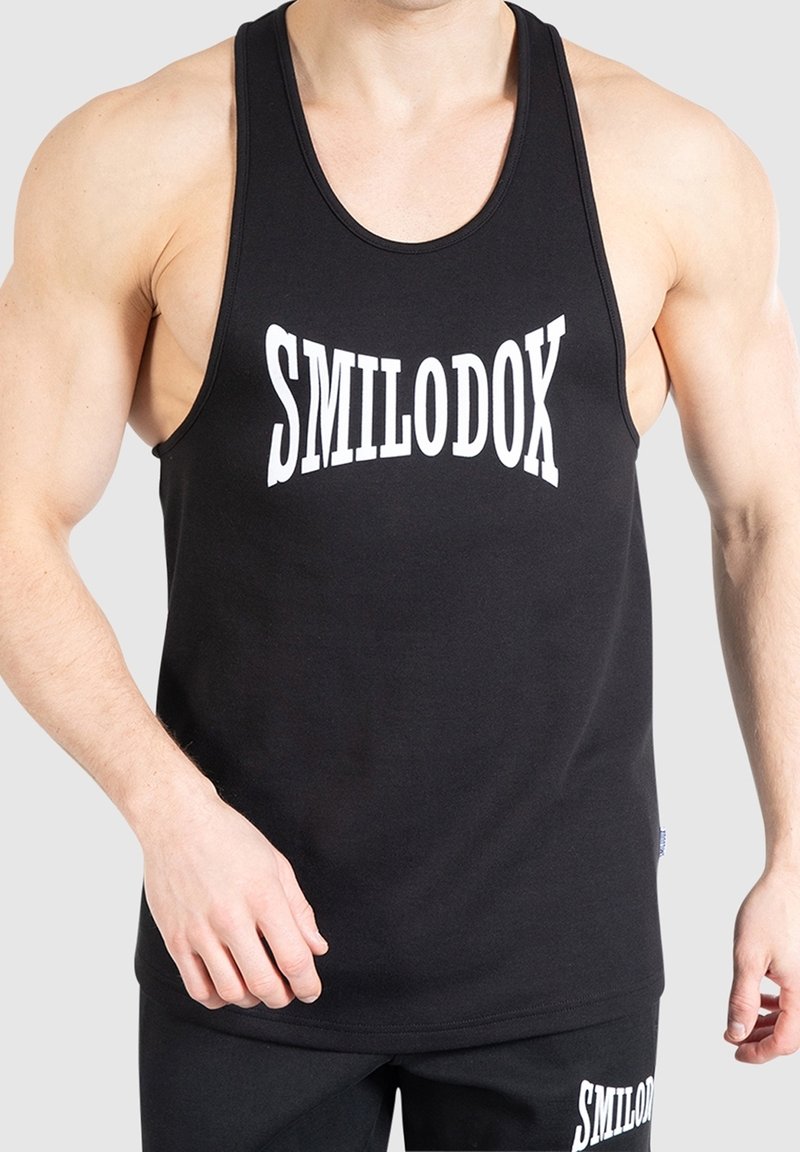 Personne musclée portant un débardeur noir et un short avec le texte blanc « SMILODOX » sur la poitrine et la cuisse.