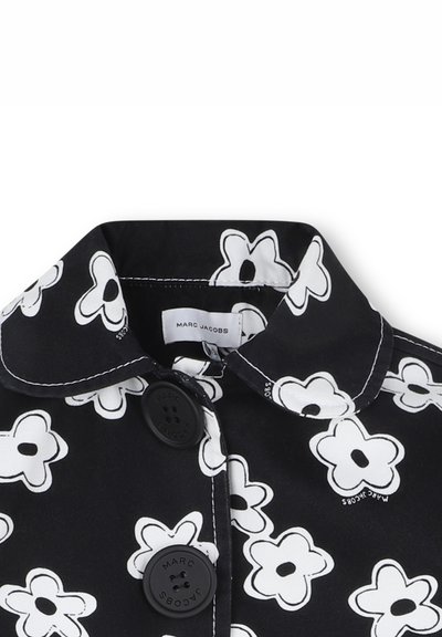 Manteau en tissu noir avec un grand motif de fleurs blanches, présentant un col arrondi et deux boutons noirs à l'avant.