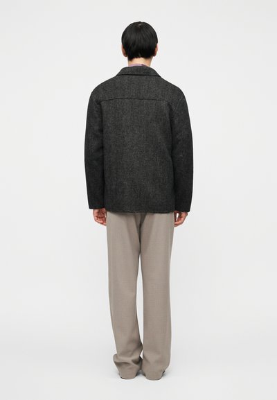 Μαύρο σακάκι από μείγμα μαλλιού με γιακά με εγκοπές και δύο πίσω σκισίματα, σε συνδυασμό με μπεζ παντελόνι φαρδύ. Λείο ύφασμα και εφαρμοστή γραμμή.