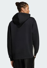 Czarna bluza z kapturem o miękkiej teksturze, z długimi rękawami i paskami po bokach. Posiada luźny krój i kieszeń typu kangur.