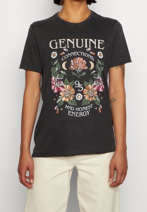 Person wearing a black t-shirt with floral design and text "Genuine Connections and Honest Energy" paired with light beige pants.