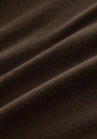 Weiches, dunkelbraunes Material mit feiner gerippter Textur und sanften Falten, die diagonale Linien über die Oberfläche ziehen.