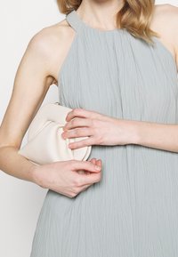 Vestido halter gris claro con un acabado texturizado, combinado con un clutch crema que presenta un diseño plegado y un sutil detalle de hardware.