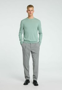 Un pull vert clair à manches longues associé à un pantalon plissé gris. La tenue présente une coupe simple, avec une texture douce et des chaussures noires.