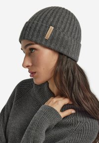 Gray knitted beanie with ribbed texture, featuring a small tan leather tag on the side and a close-fitting design.