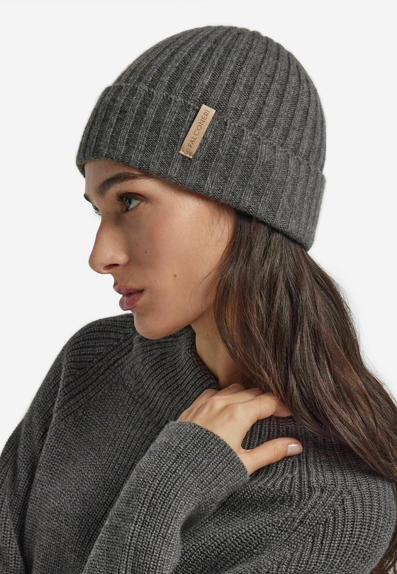 Gray knitted beanie with ribbed texture, featuring a small tan leather tag on the side and a close-fitting design.