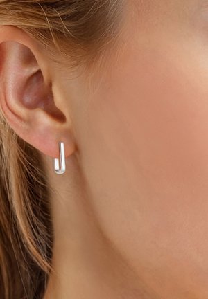 Boucle d'oreille en argent au design minimaliste, présentant une forme allongée et élégante avec une texture lisse, portée sur l'oreille d'un modèle.