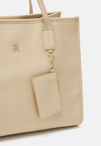 Beige schoudertas met een gladde, synthetische textuur. Voorzien van gouden accenten, inclusief een logo, en een afneembare kaarthouder met rits.