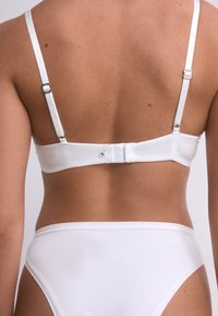 Reggiseno bianco con spalline sottili regolabili, chiusura con gancio e occhiello e texture liscia. Presenta dettagli con logo sulle spalline e sulla fascia.