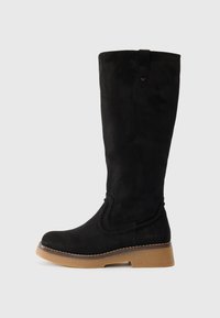 Botte noire en daim jusqu'au genou avec un embout arrondi, semelle en caoutchouc marron contrastée et coutures décoratives sur le côté. Comprend une languette de tirage.