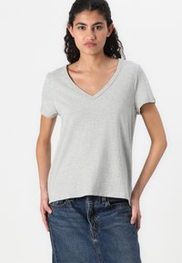 Szara koszulka V-neck z miękkiego materiału, krótki rękaw i luźny krój, noszona z niebieską dżinsową spódnicą. Czysty design, bez widocznych wzorów.