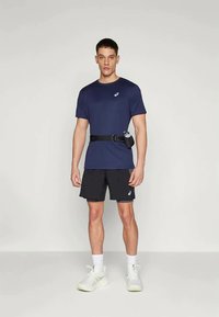 Navy blue short-sleeve shirt with logo, black shorts, and a black belt bag. Worn with white athletic shoes, standing on a plain background.