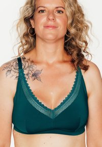 Bralette teal con un bordo in pizzo a forma di scallop lungo la scollatura a V, in tessuto morbido e senza stecche. Presenta un design semplice e senza cuciture.