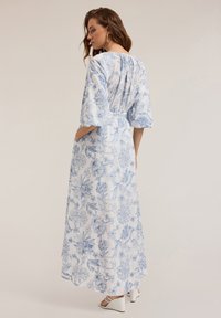 Long white dress with blue floral patterns, wide sleeves, and a cinched waist. The back features subtle pleating and side pockets.